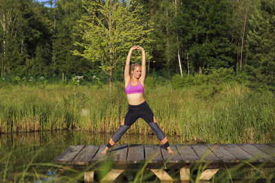 Full length portrait of woman exercising against trees on jetty