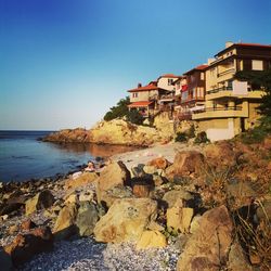 Buildings by sea against clear blue sky