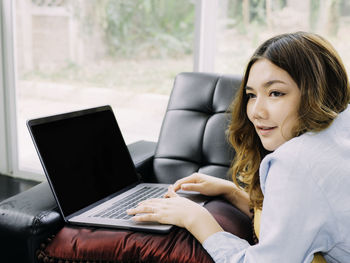 Smiling young woman using laptop while sitting on sofa