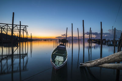 Sailboats moored in lake against sky during sunset