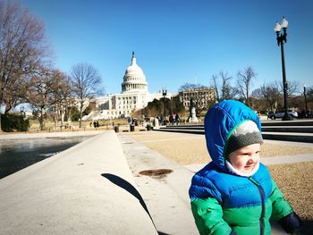 Cute toddler girl standing in park against capitol building during sunny day