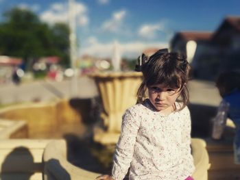 Girl looking away while standing by fountain on sunny day