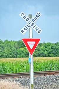 Road sign by railroad tracks against sky