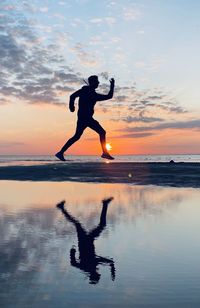 Side view of man jumping at beach against sky during sunset