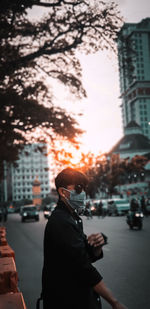 Man standing on city street against sky during sunset