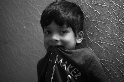 Portrait of smiling boy biting t-shirt while standing against wall