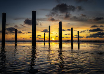 Wooden posts in sea against sky during sunset