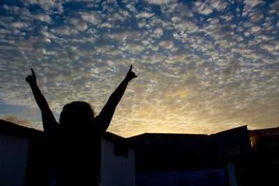 Silhouette woman standing by building against sky during sunset