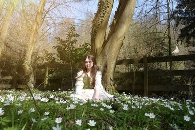 Portrait of smiling young woman sitting on land, in a flower meadow with sunlight 