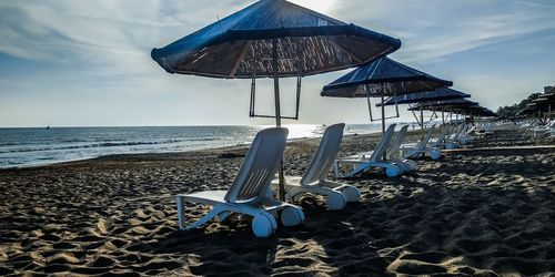 Deck chairs on beach against sky
