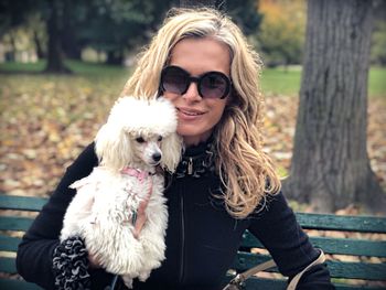 Portrait of woman with dog sitting on bench in park 