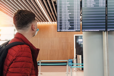 Man wearing a mask protection at an airport. looking to the screen with departure  information.