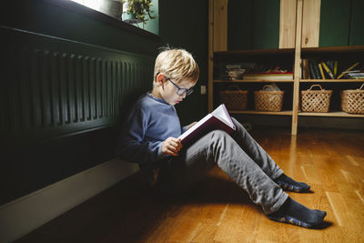 Boy reading book sitting on floor at home