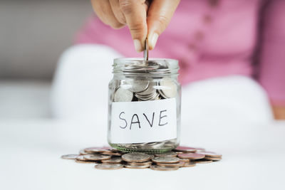 Close-up of hand holding coins in jar