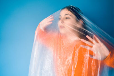 Woman covered in plastic standing against blue background