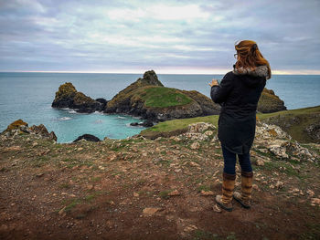 Eoman standing on cliff  by sea against sky