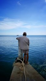 Rear view of man standing by bollard against sea