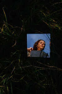 Reflection of woman on mirror amidst grass