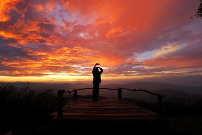 Rear view of silhouette woman standing on beach against sky during sunset