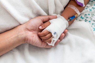 Cropped hand holding woman with iv drip on bed at hospital