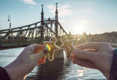 Cropped image of people holding gingerbread man against bridge