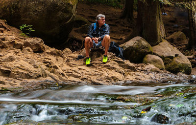 Portrait of man sitting on rock against trees