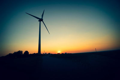 Silhouette wind turbines on field against sky during sunset