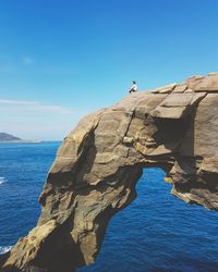 Woman sitting on cliff by sea against blue sky