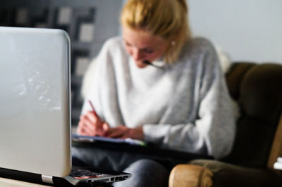 Woman writing in book by laptop at home