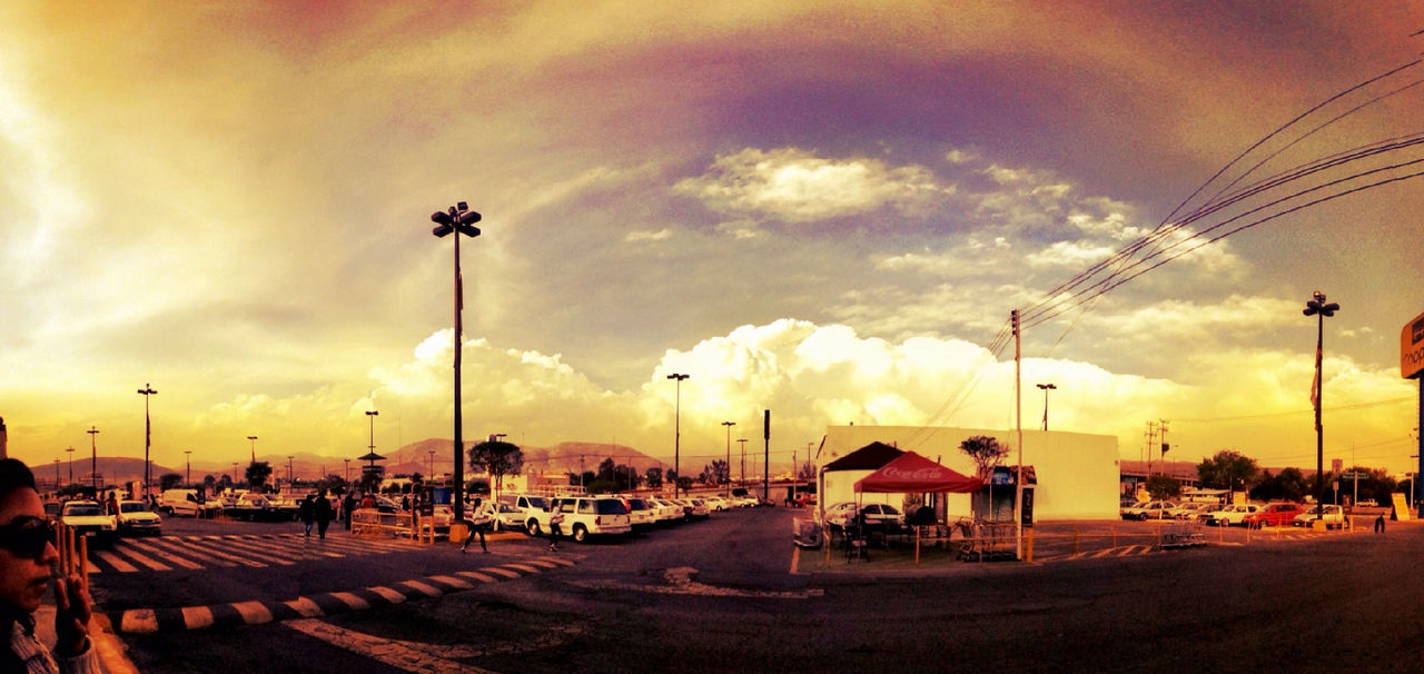 transportation, sky, car, land vehicle, mode of transport, cloud - sky, sunset, street light, street, road, building exterior, cloudy, built structure, cloud, architecture, outdoors, in a row, electricity pylon, parking lot, incidental people