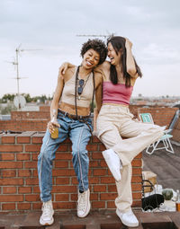 Full length of female friends laughing while sitting on rooftop
