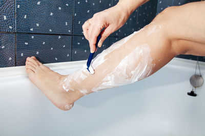 Low section of woman shaving leg in bathroom at home