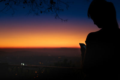 Silhouette woman using smart phone against sky during sunset