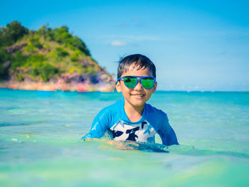 Portrait of boy wearing sunglasses swimming in sea against blue sky