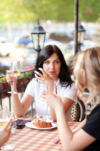 Portrait of young woman drinking glass on table at restaurant