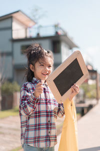 Girl holding writing slate while standing outdoors