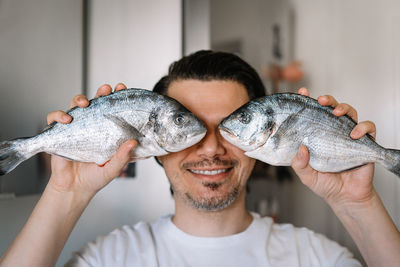 Funny portrait of man holding fish in kitchen