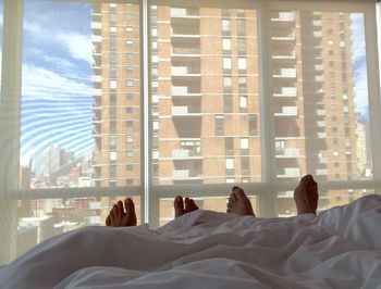 Low section of couple resting in bed against building seen through window