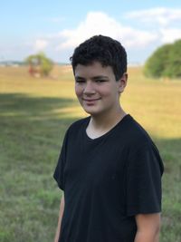 Portrait of boy standing on field against sky