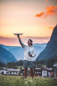 Man holding drone while standing on field against sky during sunset