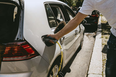 Cropped image of man's hand charging electric car at station