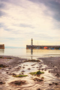 View of lighthouse on beach against cloudy sky