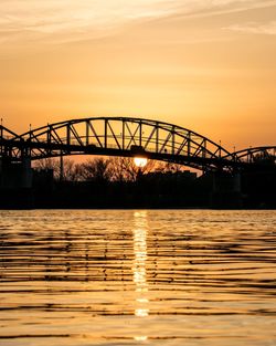 Silhouette bridge over river against sky during sunset