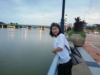 Side view portrait of smiling mature woman standing by river against sky in city