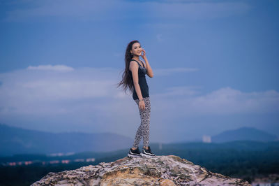 Portrait of young woman standing on rock against sky