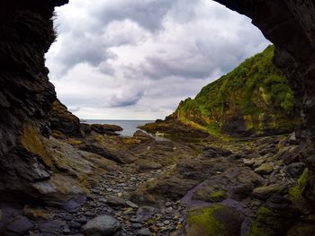 Cliff by sea against cloudy sky seen through cave