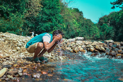 Side view of man surfing on rock in river