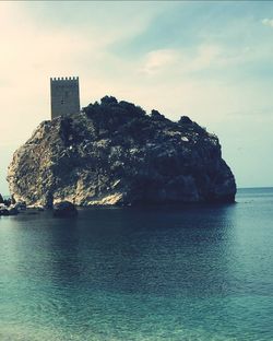 Castle on rock amidst sea against sky