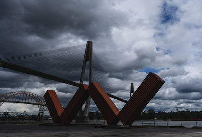 Low angle view of bridge against cloudy sky