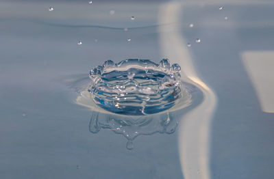 Close-up of drop splashing on water against blue background